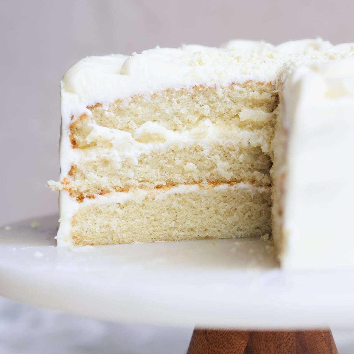 A sliced white layer cake with creamy white frosting sits on a marble cake stand, revealing its soft, fluffy interior.